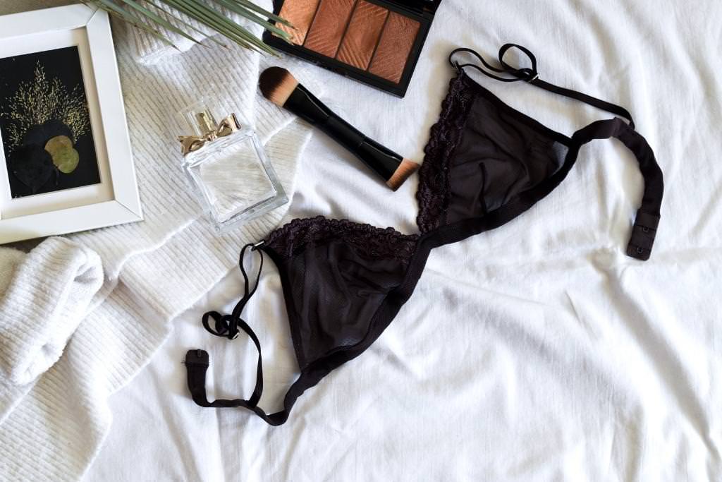 white bed with white sweater, bottle of perfume and black bra laying on it