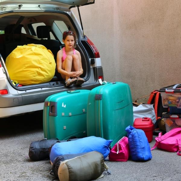 girl sitting in back of car with suitcases