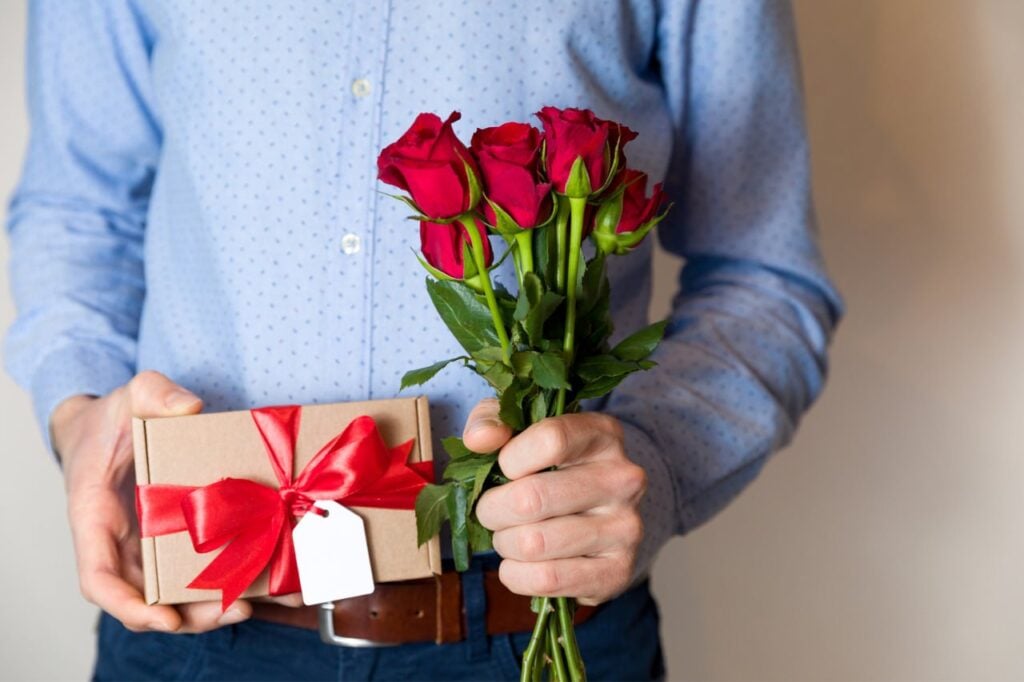 Handsome man holding red roses and romantic gift with red bow and gift tag