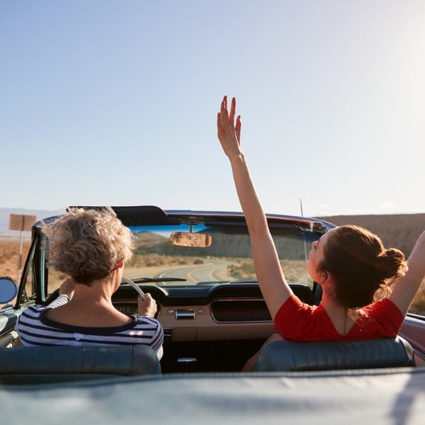 Mom driving car daughter with hands in the air