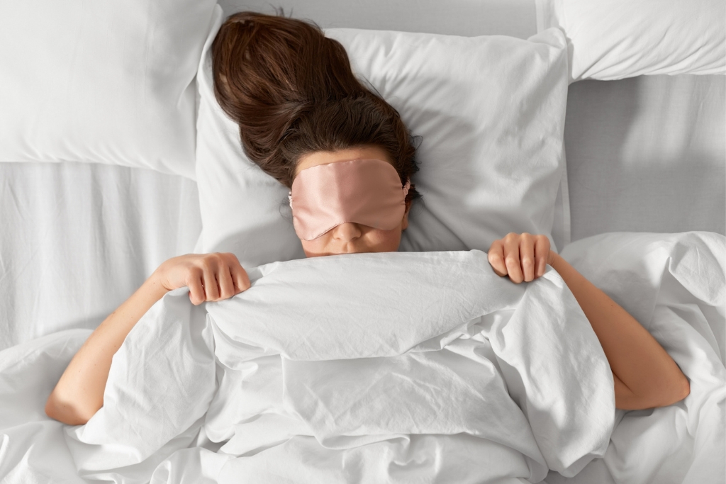 Woman with eye sleeping mask in bed under bla